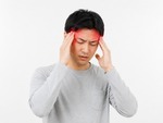 頭痛でこめかみを押さえる男性のイメージ