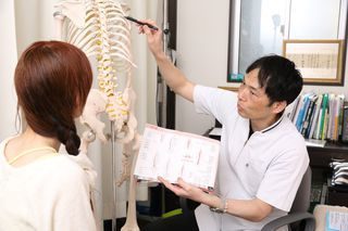 姫路市の鍼灸整骨院一心堂で、院長が骨格模型を使って患者に痛みの原因を説明しているカウンセリングの様子。