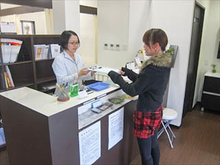 姫路市の鍼灸整骨院一心堂の受付の様子。初めて来院された患者がスタッフに案内を受け、問診票を受け取っている場面。