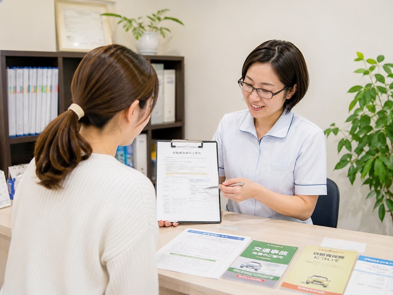 交通事故後の自賠責保険や必要書類について、受付で分かりやすく説明している様子