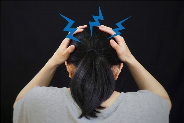 頭痛を感じ、後頭部を両手で押さえる女性